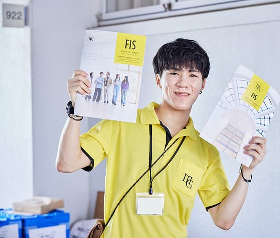 国際学部のパンフレットを持つスタッフ学生