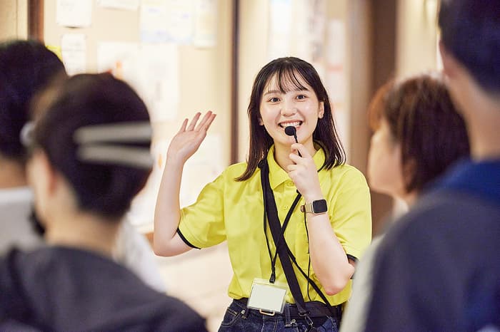 マイクを持って案内するスタッフ学生
